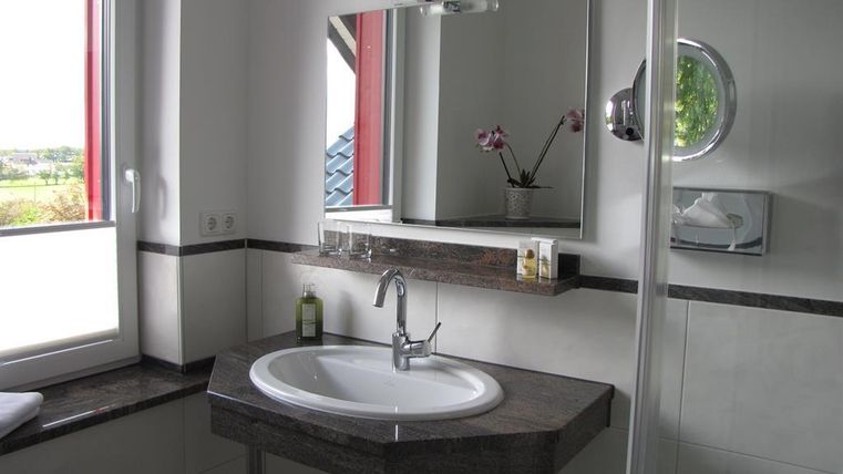 Ein modernes Badezimmer mit einem runden Waschbecken und einem großen Spiegel. Die Fenster lassen viel Licht herein und es gibt einen eleganten Duschbereich.