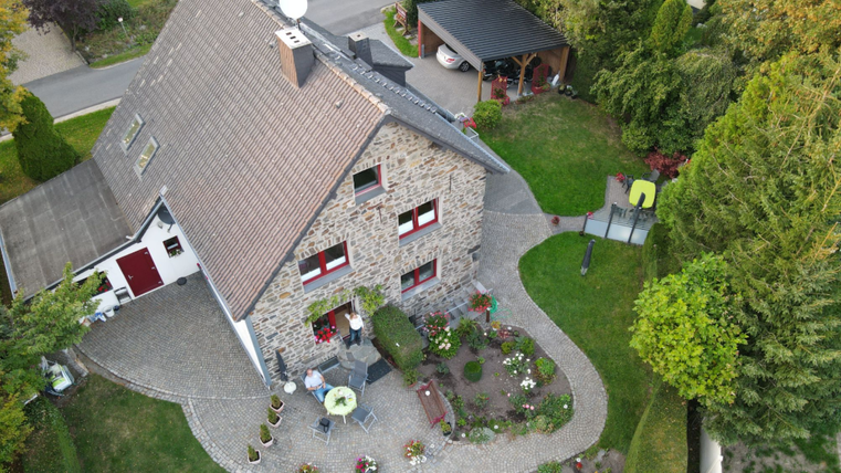 Ein schönes Haus aus Steinen mit einem gepflegten Garten. Im Vordergrund sind Sitzecken und Blumenbeete zu sehen.