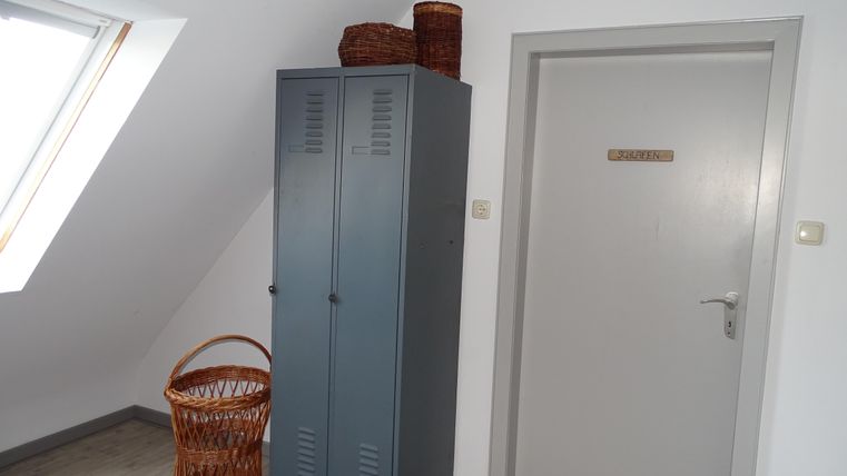 Ein heller Raum mit einer grauen Garderobe und einem weißen Tür. Neben der Garderobe steht ein geflochtener Korb.