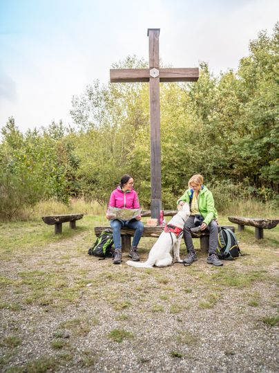 Zwei Wanderinnen mit Hund auf einer Bank am Gipfelkreuz auf der Sophienhöhe im Rheinischen Revier.