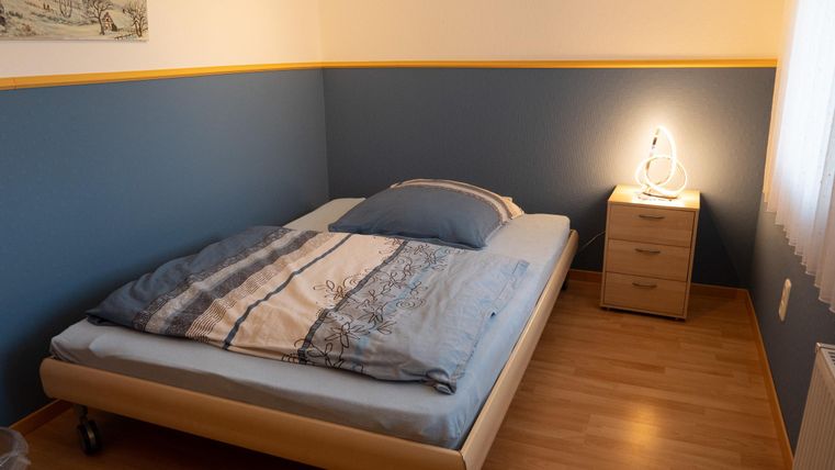 Ein gemütliches Schlafzimmer mit einem Bett und einem Nachttisch. An der Wand ist eine blaue Farbe zu sehen, die durch eine gelbe Leiste ergänzt wird.