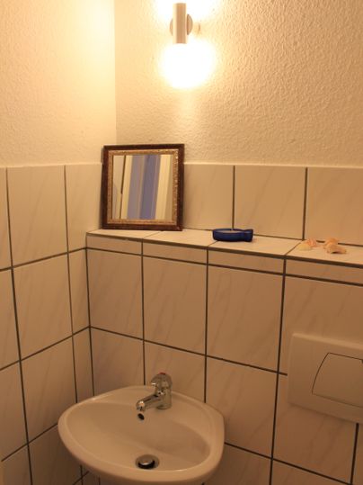 Ein kleines Badezimmer mit einem Waschbecken und einer Wandlampe. Auf der Ablage befinden sich ein Spiegel und einige kleine Gegenstände.