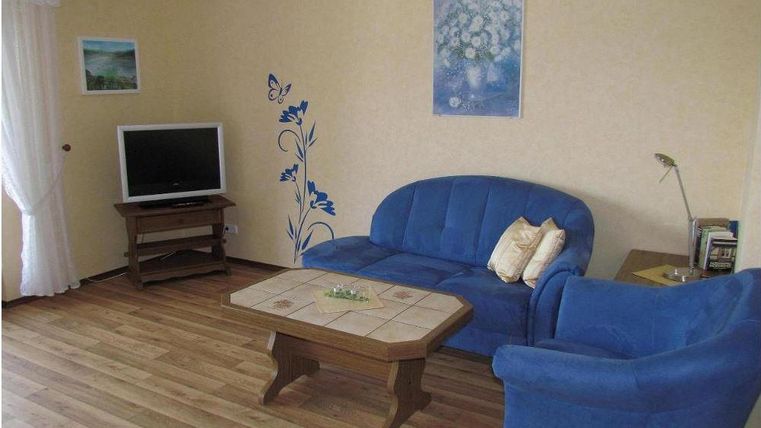 Ein gemütliches Wohnzimmer mit blauen Sofas und einem Fernseher. An der Wand sind dekorative Blumenmuster und das Zimmer hat ein warmes Ambiente.