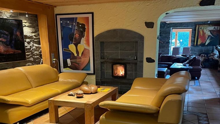 Ein gemütliches Wohnzimmer mit zwei gelben Sofas und einem Tisch. Im Hintergrund ist ein Kamin und farbenfrohe Kunstwerke an den Wänden zu sehen.