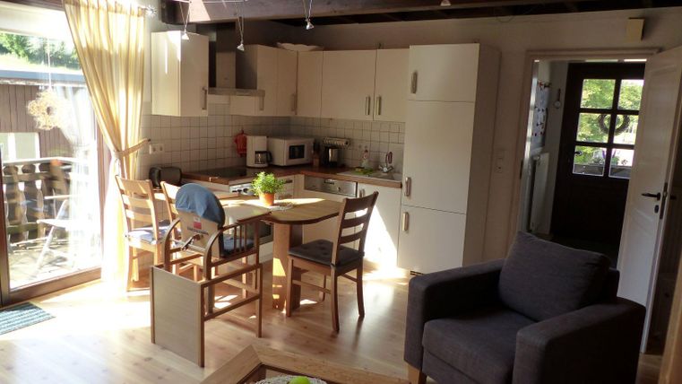 Eine helle und moderne Küche mit Essbereich und gemütlichem Sessel. Große Fenster sorgen für viel Tageslicht und vermitteln ein einladendes Ambiente.