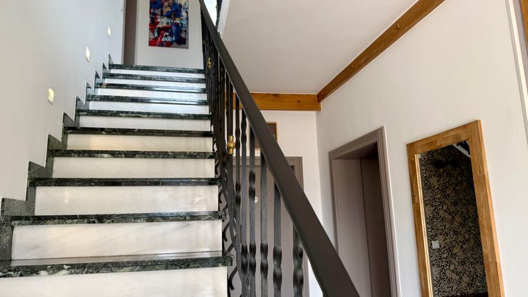 Eine helle Treppe mit marmorierten Stufen und einem eleganten Geländer. An der Wand hängt ein farbenfrohes Kunstwerk und ein Spiegel ist zu sehen.