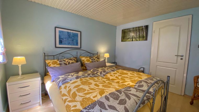 Ein gemütliches Schlafzimmer mit einem großen Bett und bunten Kissen. Die Wände sind in sanften Farben gestrichen und es gibt eine Nachttischlampe.