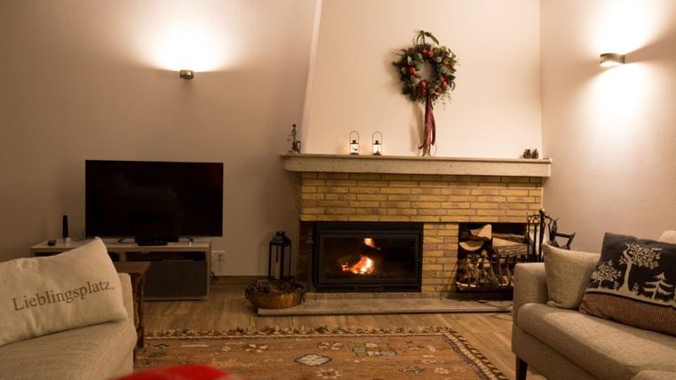 Ein gemütliches Wohnzimmer mit einem Kamin und einem Fernseher. Die Weihnachtsdekoration und ein warmer Teppich schaffen eine einladende Atmosphäre.