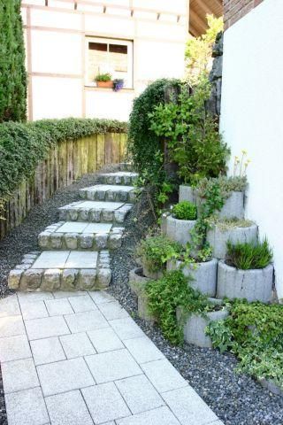 Ein schöner Gartenweg mit Steinstufen und bepflanzten Blumenbeeten. Der Weg führt zu einem Haus und ist von grünen Pflanzen umgeben.