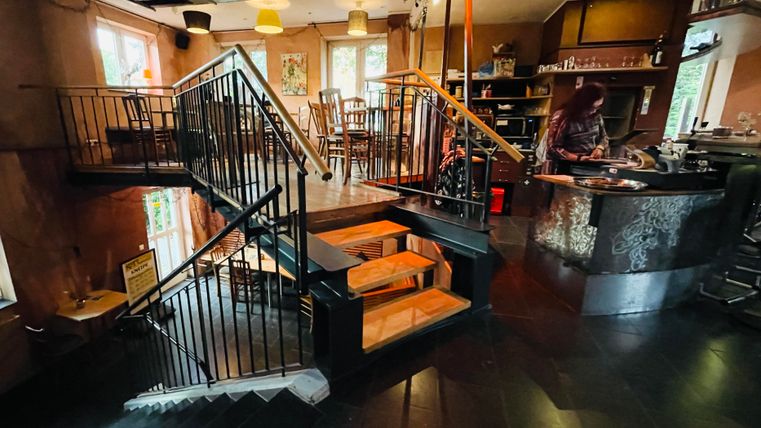 Ein stilvolles Café mit einer Treppe und einem Bartresen. Die Einrichtung ist gemütlich und hell.