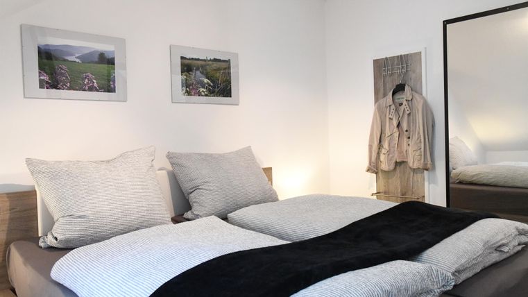 Ein gemütliches Schlafzimmer mit einem großen Bett und weichen Kissen. An der Wand hängen Bilder und ein Spiegel steht neben dem Bett.