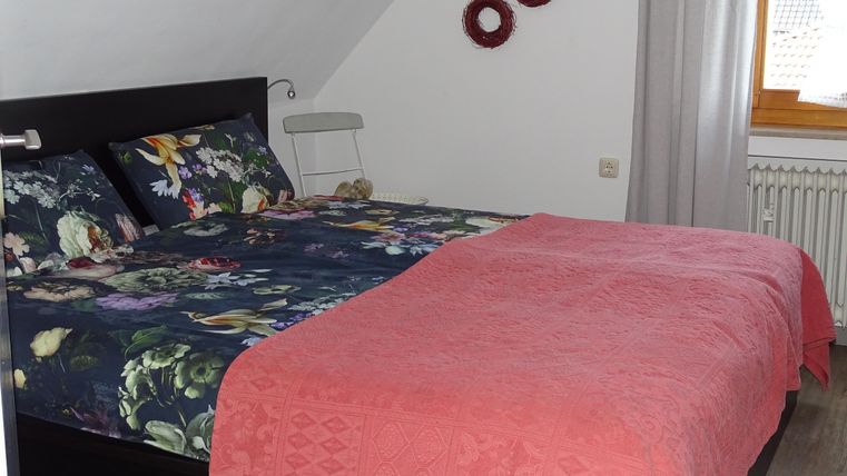Ein gemütliches Schlafzimmer mit einem großen Bett und bunten Bettwäsche. Die Wände sind mit dekorativen Elementen geschmückt und es gibt viel Tageslicht.