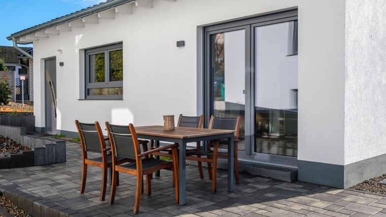 Ein modernes Haus mit einem Außenbereich. Ein Tisch mit Stühlen steht auf der Terrasse.
