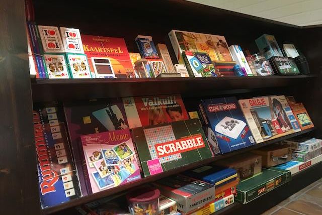 Ein Regal mit verschiedenen Brettspielen und Kartenspielen. Die Spiele sind bunt verpackt und umfassen Klassiker wie Scrabble und Memory.