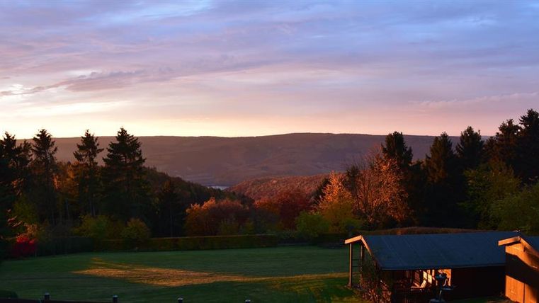 Eine malerische Landschaft mit sanften Hügeln und Bäumen bei Sonnenuntergang. Der Himmel hat warme Farben, die die Szenerie beleuchten.