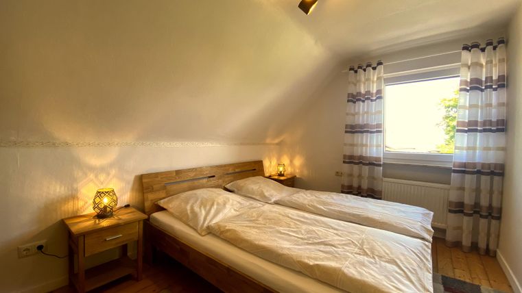 Ein gemütliches Schlafzimmer mit zwei Einzelbetten und warmem Licht. Die großen Fenster lassen viel Tageslicht herein und bieten einen Blick ins Freie.