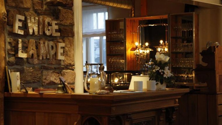 Ein gemütlicher Empfangsbereich mit einem Holztheken und einer Vitrine im Hintergrund. An der Wand steht der Schriftzug "EWIGE LAMPE".